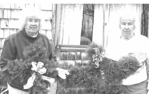 Elizabeth Brown and Katherine Vaillancourt, twin sisters, each holding an evergreen wreath outside a shingled house in Cabot, Vermont.